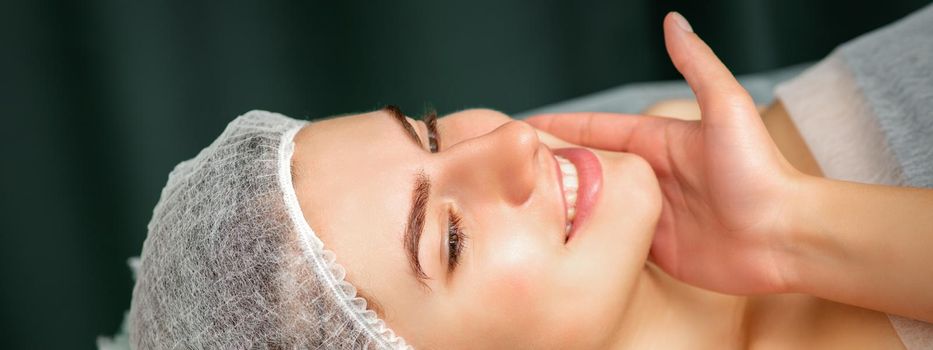 Doctor examining the beautiful face of young smiling woman in beauty clinic