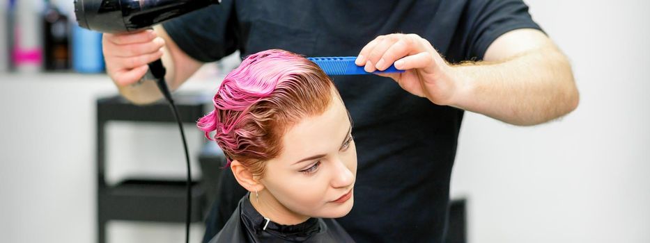 A hairdresser is drying the pink hair of the young woman in a beauty salon