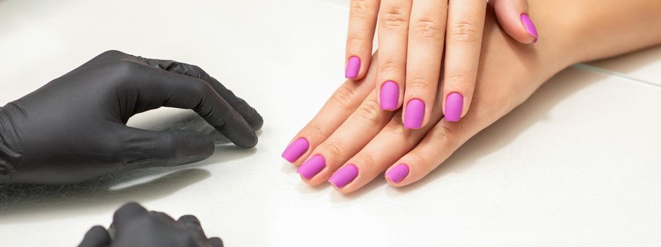 Beautiful fingers with purple nails after nail polish procedure in manicure salon