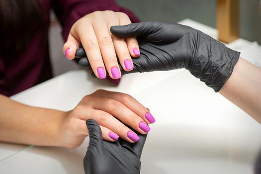 Examination of manicured fingernails. Hands of manicure master in black gloves examining female pink nails in manicure salon