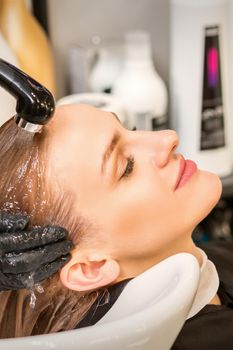 Young caucasian blonde woman having hair washed in the sink at a beauty salon