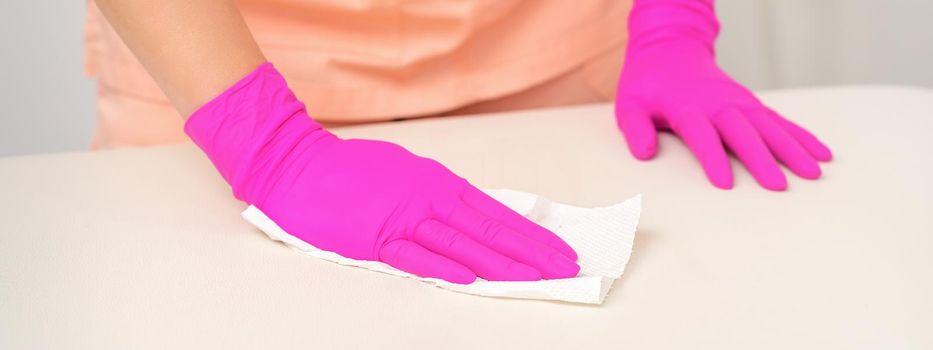 Close up of hands in rubber protective pink gloves cleaning the white surface with a white rag