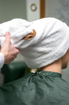 A hairdresser is wrapping the wet hair of the young woman in a towel after washing at the beauty salon