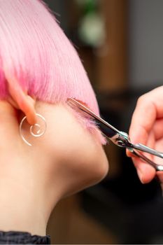 Cutting female hair. Hand of a hairdresser cutting short pink hair of young white woman at the hair salon