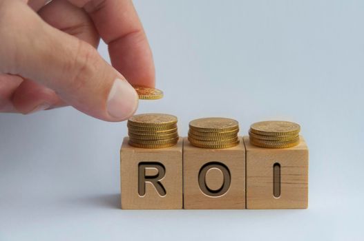 Hand placing coins on wooden blocks with ROI text engraved on wooden cubes - Business and Investment concept.