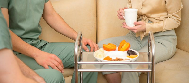 Young caucasian woman consulting with two masseurs during tea with dried fruit in the massage spa