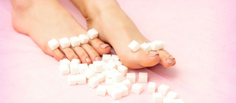 Sugar cubes lying in a row on female feet on pink background with copy space, depilation concept