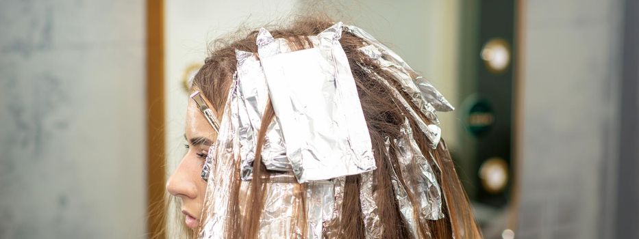Hair foiled during hair dyeing of a young woman in hair salon close up