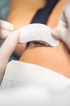 The beautician is gluing a patch under her eyes, before the procedure of eyelash extension. Artificial extended eyelashes