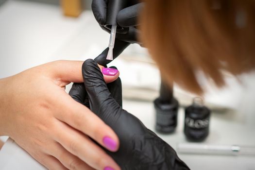 Painting nails of a woman. Hands of Manicurist in black gloves applying pink nail polish on female Nails in a beauty salon