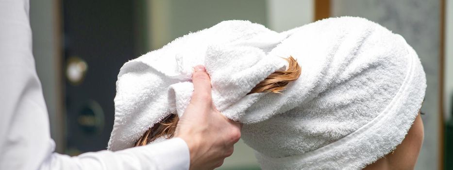 A hairdresser is wrapping the wet hair of the young woman in a towel after washing at the beauty salon