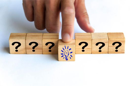 Hand pushing wooden cube block with light bulb surrounded by questions marks. Solution and idea concept.