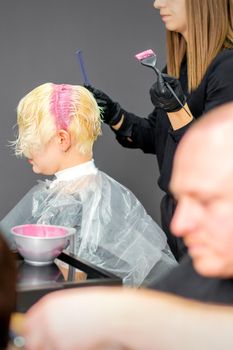 Coloring female hair in the hair salon. Young woman having her hair dyed by beautician at the beauty parlor