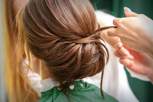 Professional hairdresser doing hairstyle for a beautiful brunette young woman with long hair. Concept of fashion and beauty