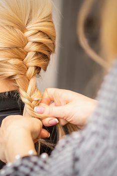 Braiding braid. Hands of female hairdresser braids long braid for a blonde woman in a hair salon