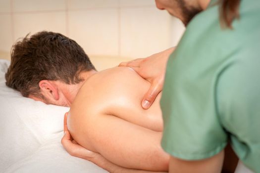 Physiotherapist giving shoulder massage to man in hospital