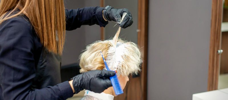 Coloring female hair in the hair salon. Young woman having her hair dyed by beautician at the beauty parlor