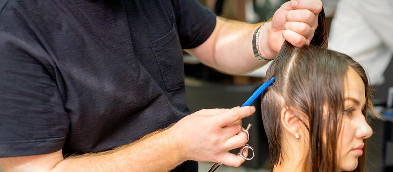 Hairdresser divides female hair into sections with comb holding hair with her hands in hair salon close up