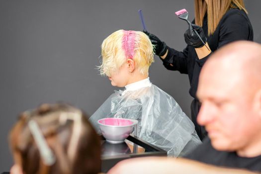 Coloring female hair in the hair salon. Young woman having her hair dyed by beautician at the beauty parlor