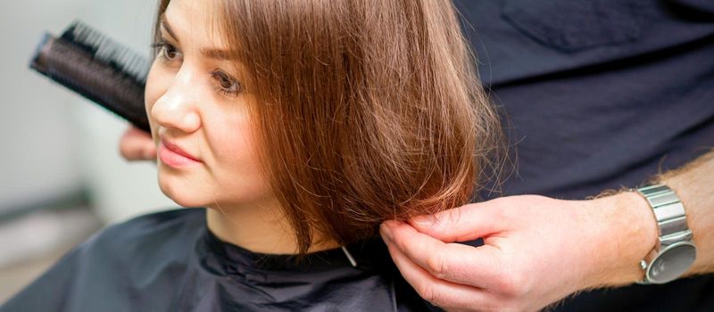 Styling female hair. Male hairdresser makes hairstyle for a young woman in a beauty salon