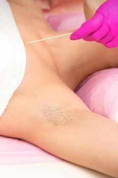 Hand in glove with spatula depilates female hairy armpit in a spa