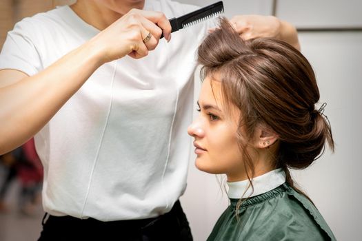 Professional hairdresser doing hairstyle for a beautiful brunette young woman with long hair. Concept of fashion and beauty