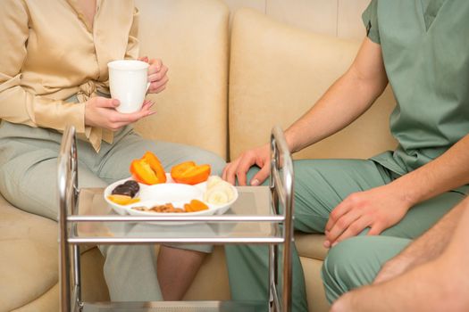 Young caucasian woman consulting with two masseurs during tea with dried fruit in the massage spa