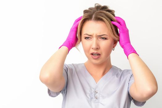 The emotionally shocked young female medical worker holding hands on her head fell into panic on white background, infection, epidemic, virus, and disease concept