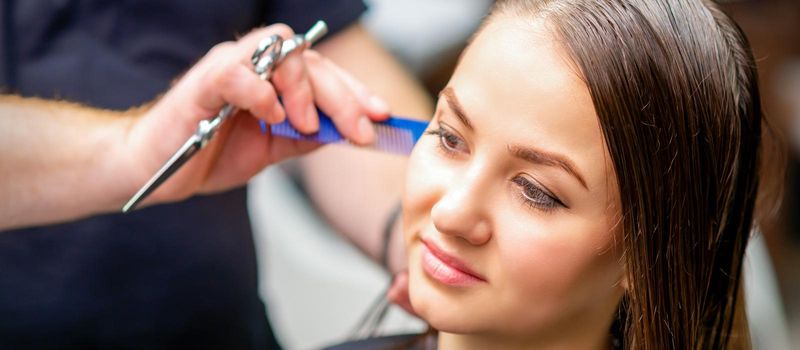 Styling female hair. Male hairdresser makes hairstyle for a young woman in a beauty salon