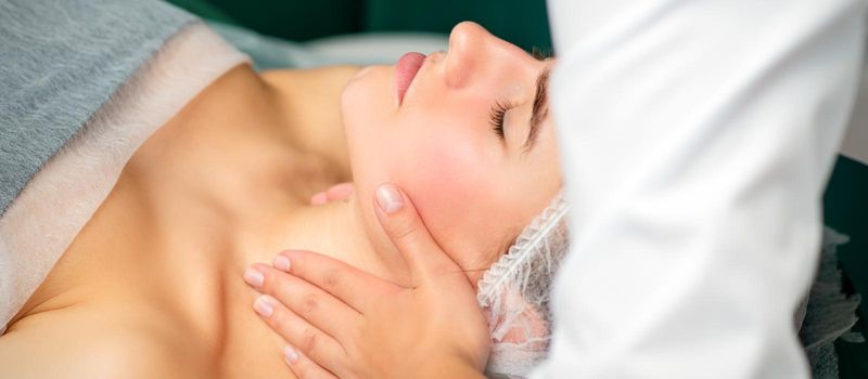 Massaging female neck. Young caucasian woman receiving neck massage relaxing in spa salon