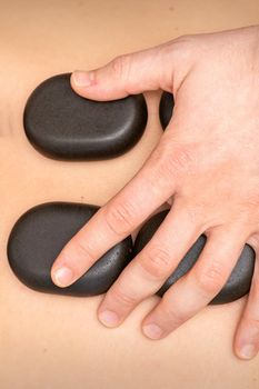 Hot stone massage therapy. Caucasian young man getting a hot stone massage on back at spa salon