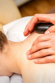 Hot stone massage therapy. Caucasian young woman getting a hot stone massage on back at spa salon