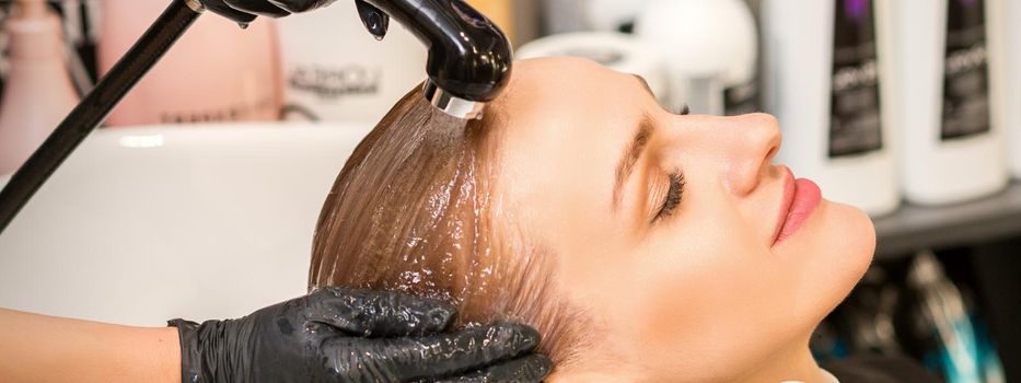 Young caucasian blonde woman having hair washed in the sink at a beauty salon