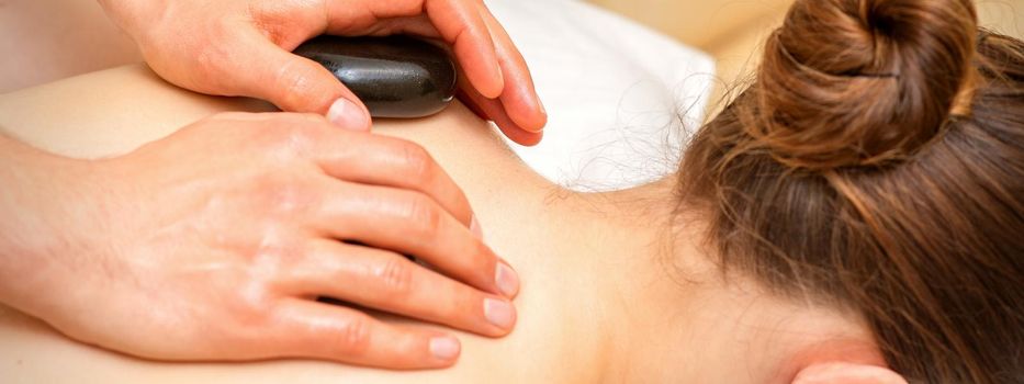 Hot stone massage therapy. Caucasian young woman getting a hot stone massage on back at spa salon