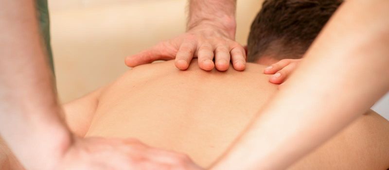 Young man receiving back massage in four hands in spa beauty salon