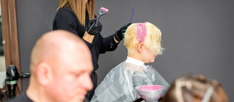 Coloring female hair in the hair salon. Young woman having her hair dyed by beautician at the beauty parlor