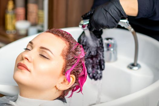 Washing dyed female hair. Professional hairdresser washes pink color paint off of a customer. Young caucasian woman having her hair washed in a beauty salon