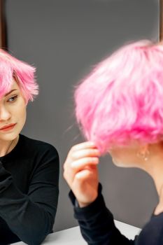 Beautiful young caucasian woman looking at her short pink hair in a mirror