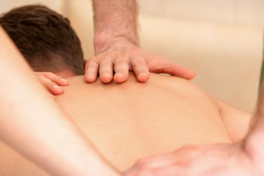 Young man receiving back massage in four hands in spa beauty salon