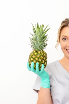 Beautiful smiling beautician holding fresh pineapple and cover her eye with lollipop over white background. Skincare cleansing eco organic