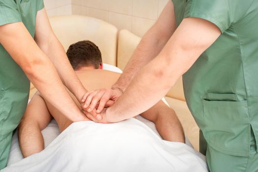 Young man receiving back massage in four hands in spa beauty salon