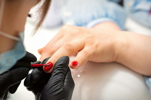 Painting nails of a woman. Hands of Manicurist in black gloves applying red nail polish on female Nails in a beauty salon
