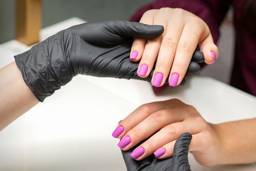 Examination of manicured fingernails. Hands of manicure master in black gloves examining female pink nails in manicure salon