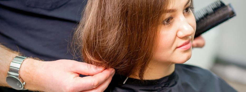 Styling female hair. Male hairdresser makes hairstyle for a young woman in a beauty salon