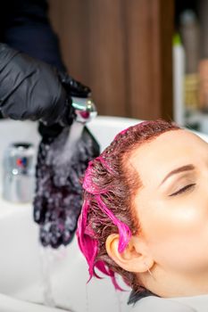 Washing dyed female hair. Professional hairdresser washes pink color paint off of a customer. Young caucasian woman having her hair washed in a beauty salon