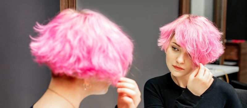 Beautiful young caucasian woman looking at her short pink hair in a mirror