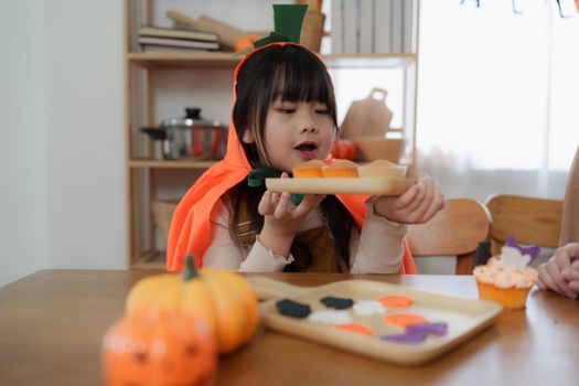 Young girl and mother at Halloween making treats and cupcake on table. Happy Halloween day.