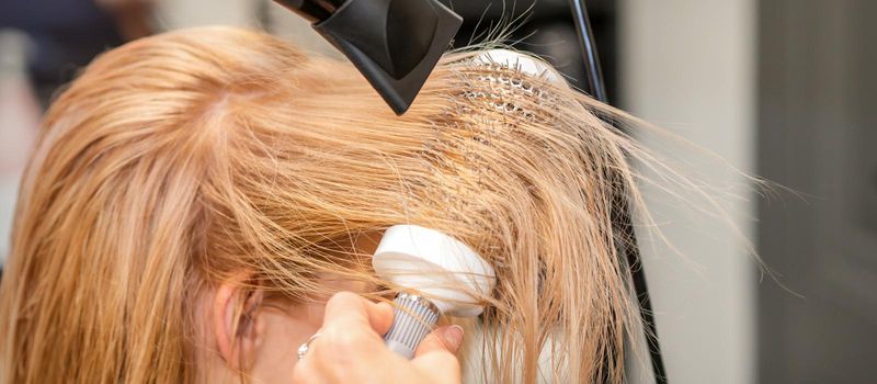 Hairdresser hand drying blond hair with a hairdryer and round brush in a beauty salon
