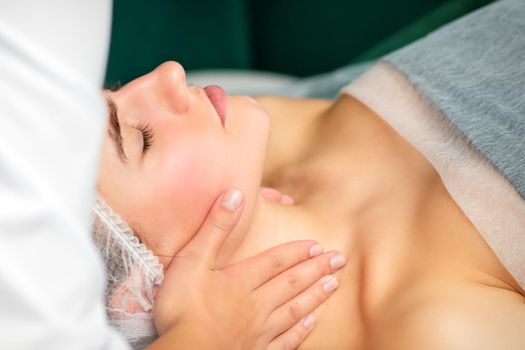 Massaging female neck. Young caucasian woman receiving neck massage relaxing in spa salon