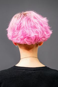 Back of female head with curly short pink hair against the dark background